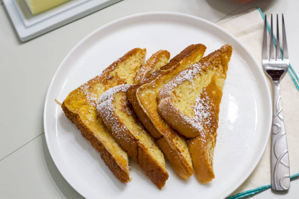 Four triangles of Texas toast french toast on a white plate, there is a fork nest to the plate.