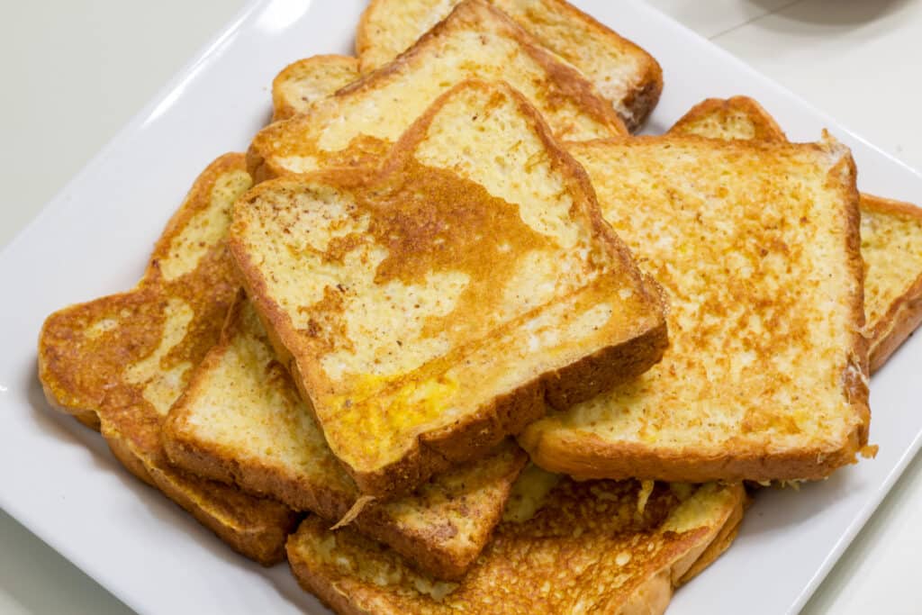A white plate with several pieces of french toast on it.