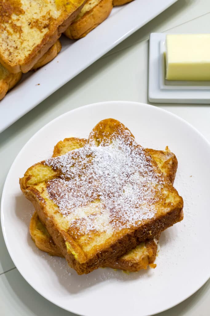 Two pieces of french toast on a white plate, there is powdered sugar on the top.