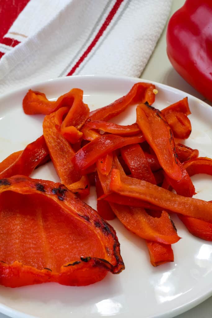 One half and some strips of roasted red peppers on a white plate.