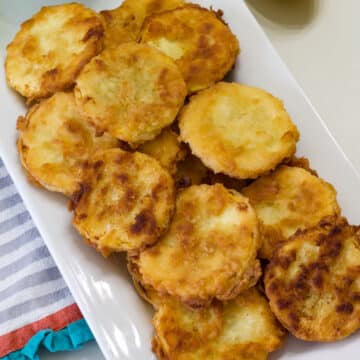 Overhead view of several fried squash rounds on a white plate.