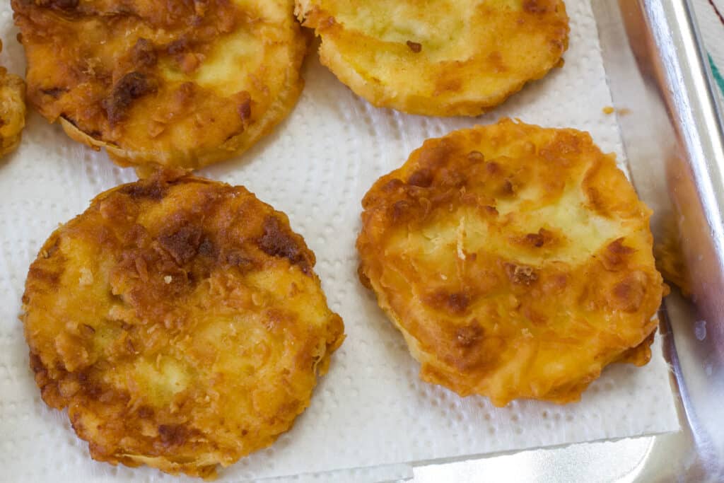 Four fried summer squash rounds on a paper towel lined baking sheet.