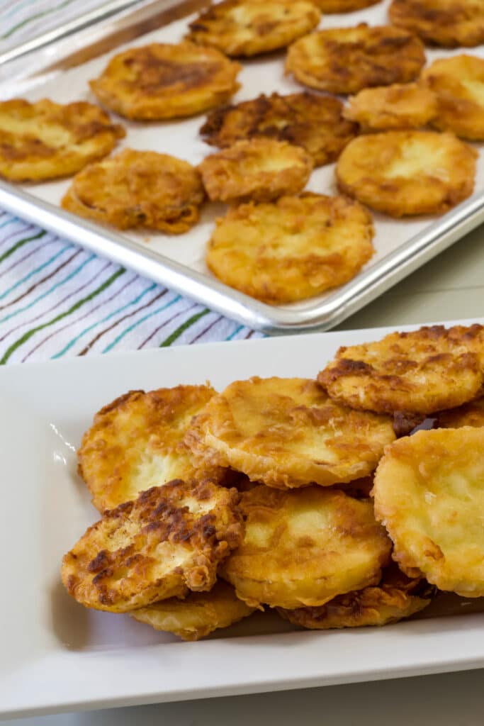 A plate of fried yellow squash in the foreground and baking sheet with squash on it in the background.