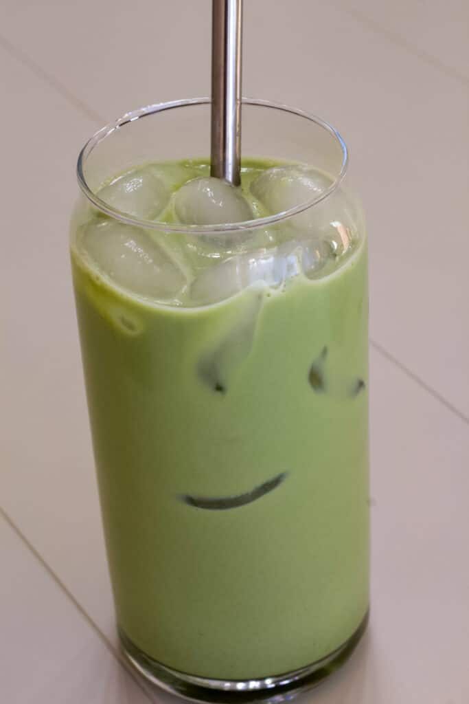 Close up shot of one glass of iced matcha tea latte with a silver straw in it.