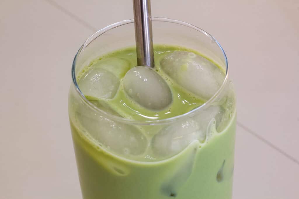 Top view of the glass of iced matcha latte with a silver straw in it.