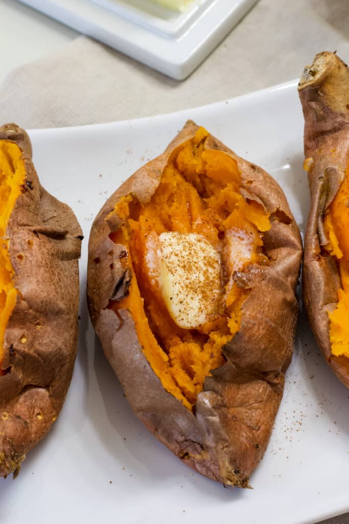 A cooked sweet potato with a pat of butter and sprinkle of cinnamon on it.