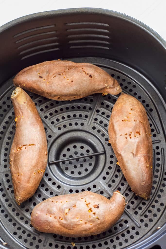 Four baked sweet potatoes in the air fryer basket.