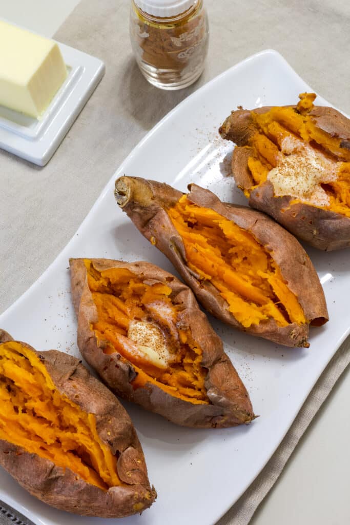 Four air fried sweet potatoes that are cut open tow have butter and cinnamon and two are plain.