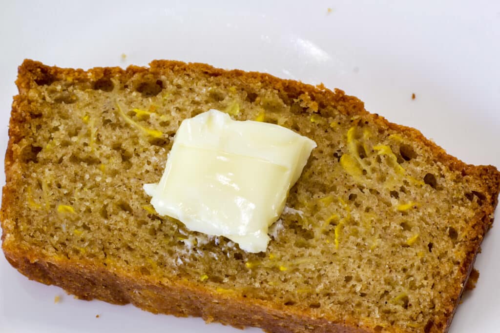 Close up shot of a cut piece of squash bread with a pat of butter on it.