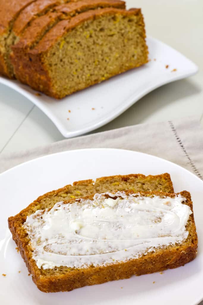A slice of squash bread with butter spread on it in the foreground and the rest of the loaf in the background.