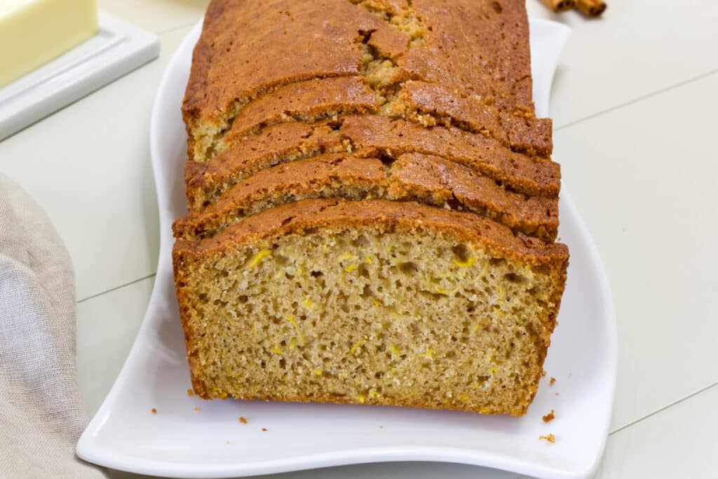 A cut loaf of Yellow Summer Squash Bread on a white plate and a partially visible stick of butter on a white butter dish nearby.