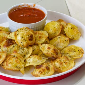 A plate that has fried ravioli and a small bowl of dipping sauce on it.