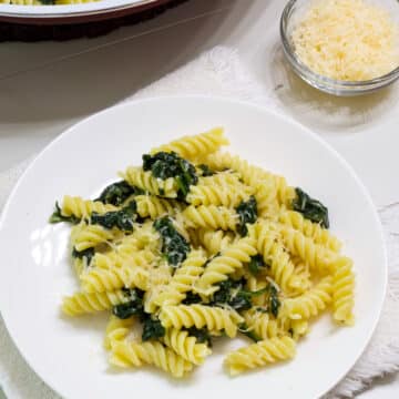 One serving of Easy Garlic Butter Pasta and Sautéed Spinach on a white plate.