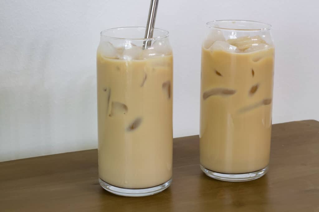 Two glasses of Easy Homemade Starbucks Iced Vanilla Coffee, one has a silver metal straw and the other one doesn't.