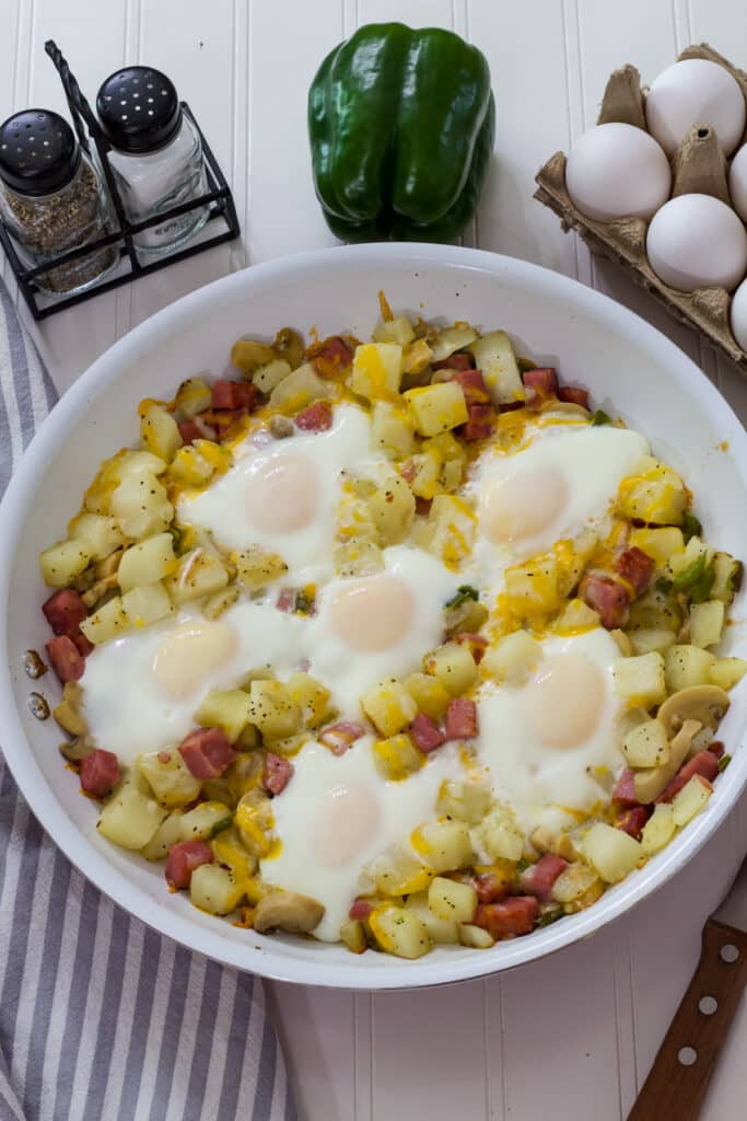 The finished Egg Ham Potato Breakfast Skillet with salt and pepper shakers, a green pepper and some eggs near it.