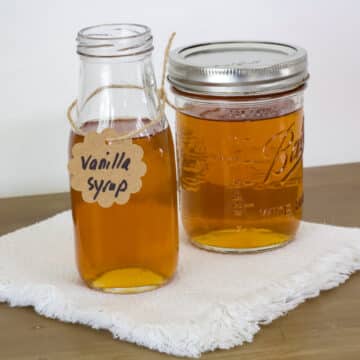 The small bottle and mason jar filled with vanilla syrup sitting on a cream colored napkin.