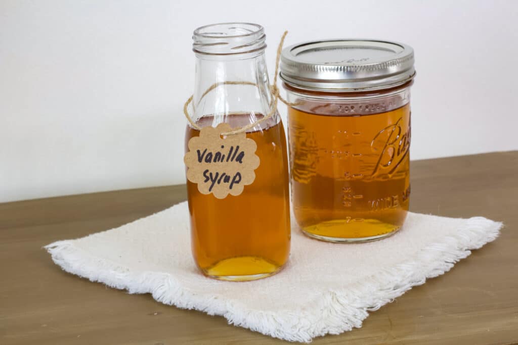 A small glass bottle and a mason jar full of the simple vanilla syrup, they are sitting on a cream colored napkin.