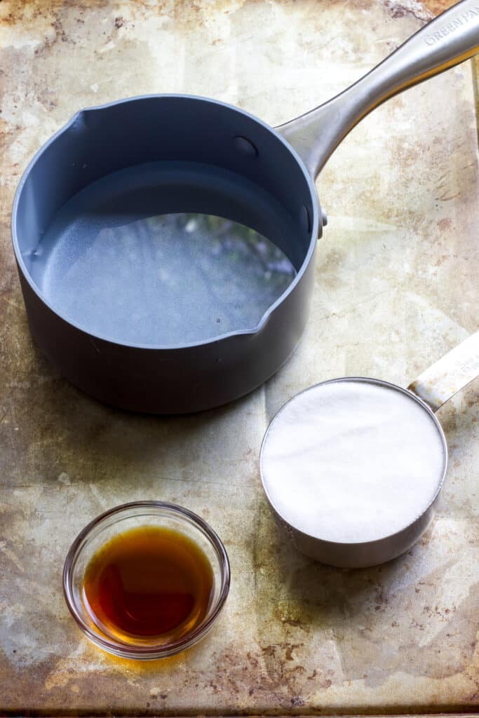 The water in a small saucepan, the pure vanilla extract and white sugar in small glass bowls.