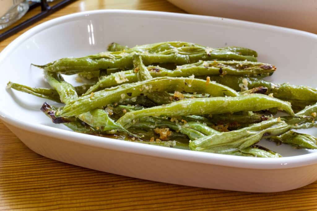 One serving of Roasted Green Beans with Paremasan Cheese on a small white rectangular plate.
