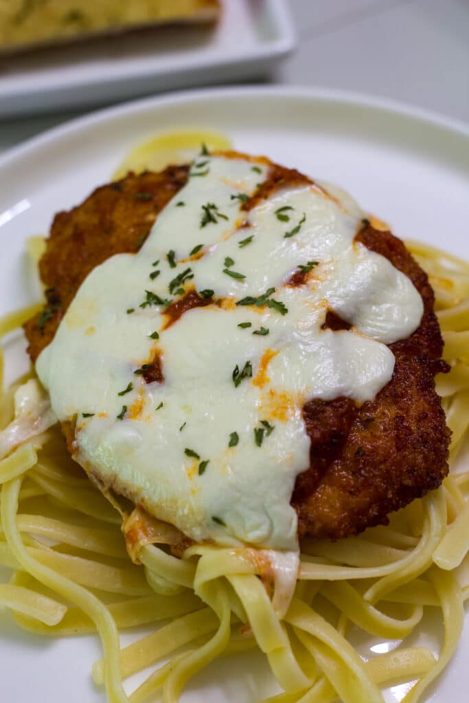 One piece of crispy chicken Parmesan on a bed of cooked fettucini.