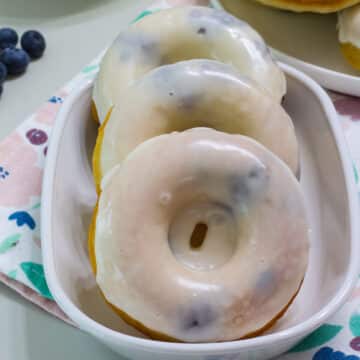 Feature image of three glazed blueberry donuts on a plate.