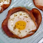 Close up view showing one baked ham and cheese egg cup in a turquoise muffin pan.
