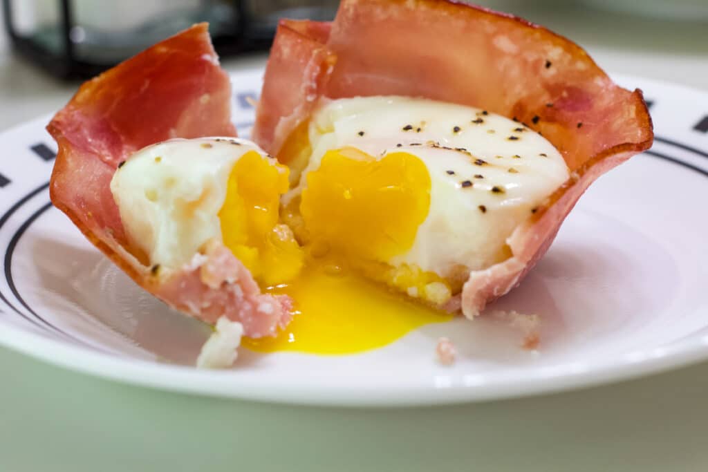 One ham, egg, and cheese cup that is cut open so the runny yolk is visible.