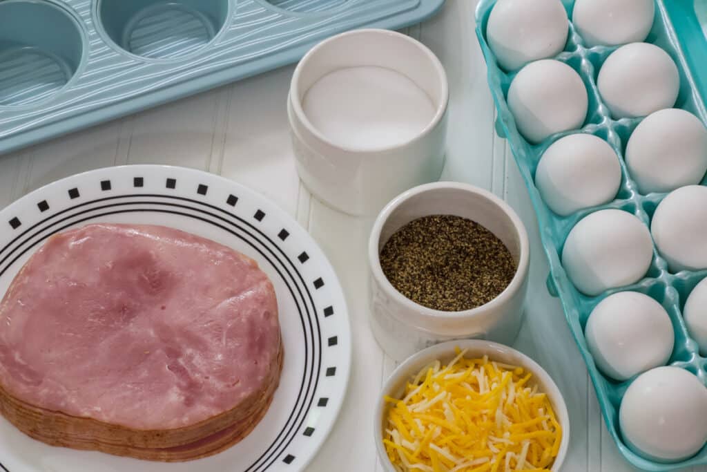 A stack of sliced ham, a dozen eggs and small bowls of cheese, salt and pepper that are needed to make the recipe.