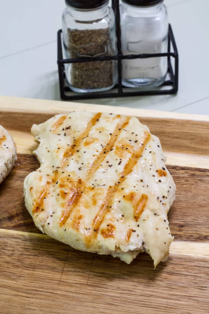 One cooked boneless chicken breast resting on a wooden cutting board.