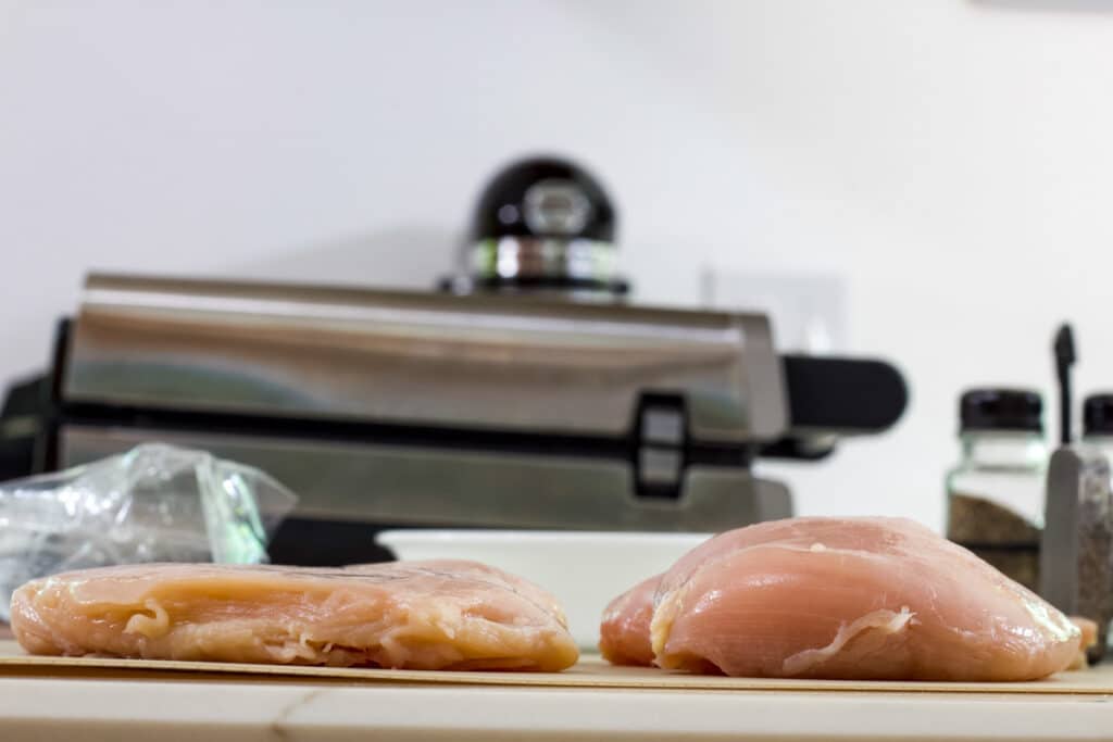 Two raw chicken breasts, one has been pounded to an even 1" thick and the other hasn't.