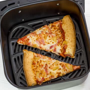 Two slices of pizza in the air fryer basket before they have been reheated.