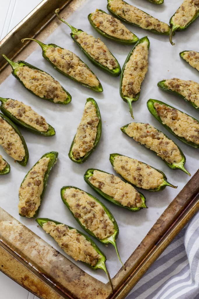 A parchment paper lined baking sheet with many cooked Stuffed Jalapenos on it.