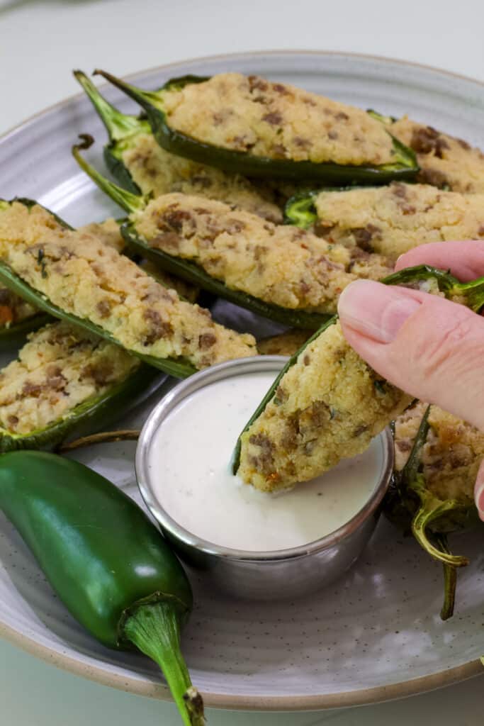 One single Stuffed Jalapeno being dipped into ranch dressing, there are many others in the background.