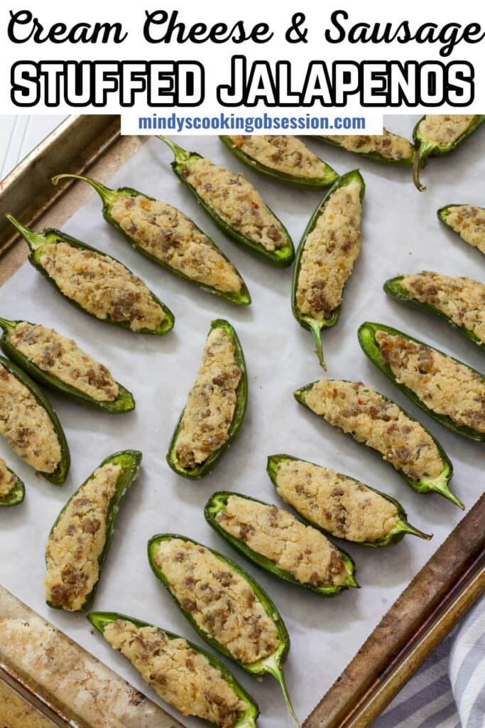 A sheet pan full of baked cream cheese and sausage stuffed jalapenos, the recipe title is in text at the top.