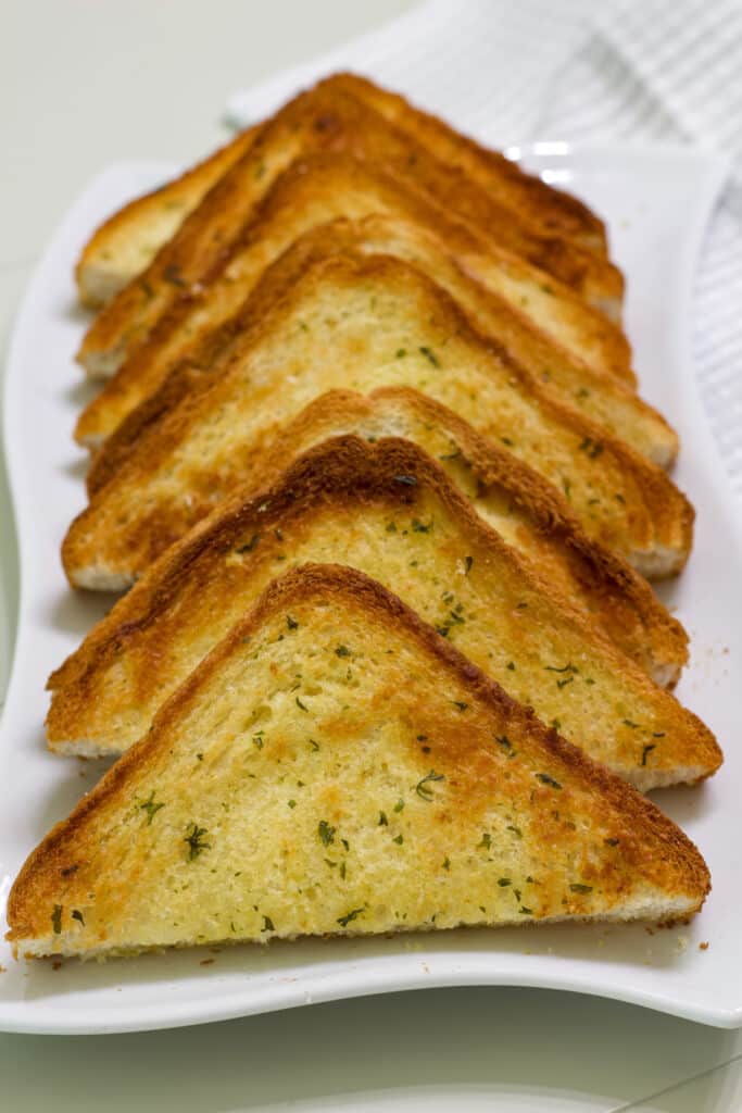Air fried garlic toast cut in half lined up on a white serving plate.