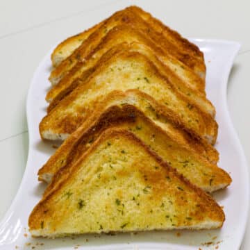 The feature image of many four pieces of garlic Texas toast that were cut in half diagonally and are lined up on a white plate.