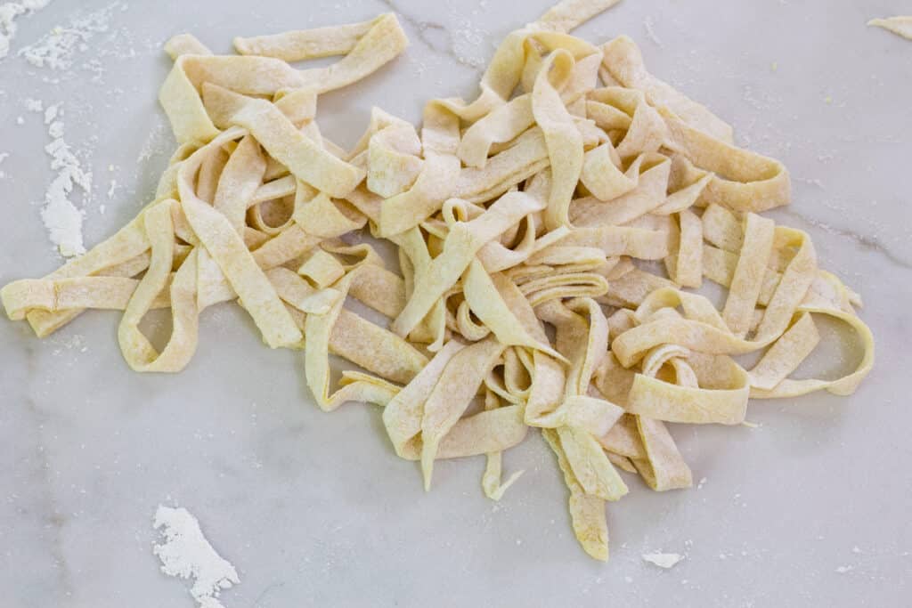 A pile of raw pasta that was just cut on a marbled quartz counter top.