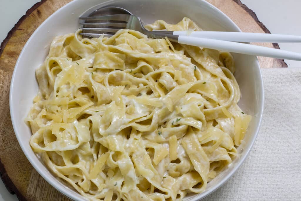 A white bowl that is filled with pasta that was boiled and then tossed in a creamy garlic Parmesan sauce.