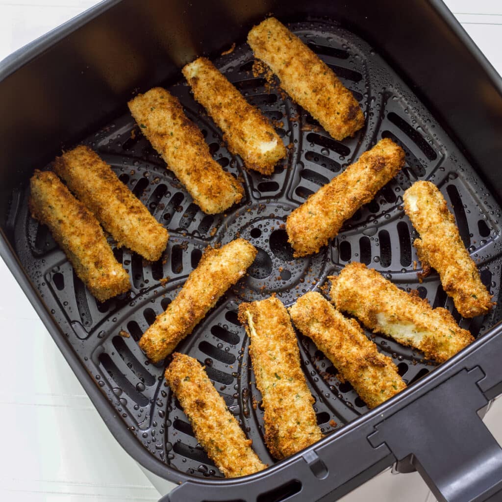 Feature image of ten cooked zucchini fries in the air fryer basket.