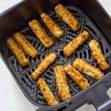 Feature image of ten cooked zucchini fries in the air fryer basket.