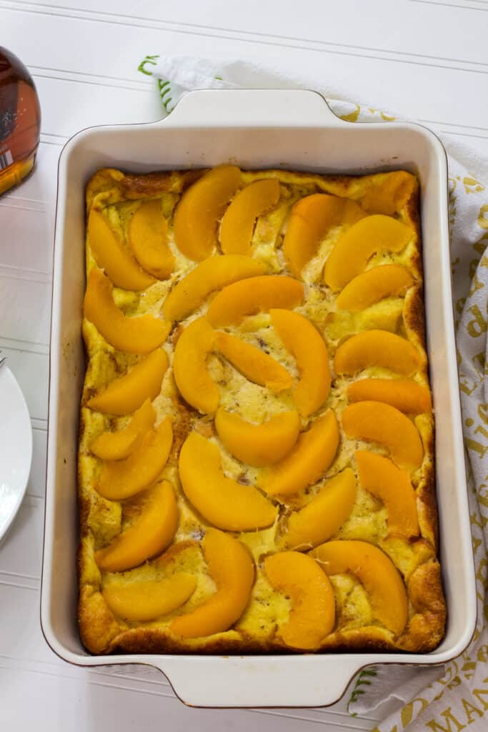 The entire baked peach French toast casserole in a cream colored oblong baking dish.