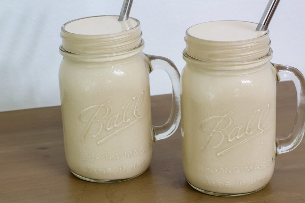 Two servings of frosted coffee in mason jar mugs with silver straws in them.