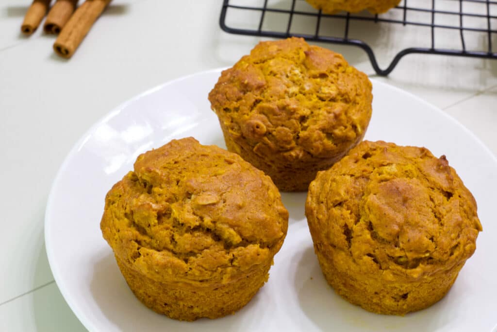 Three pumpkin oatmeal muffins on a white plate.