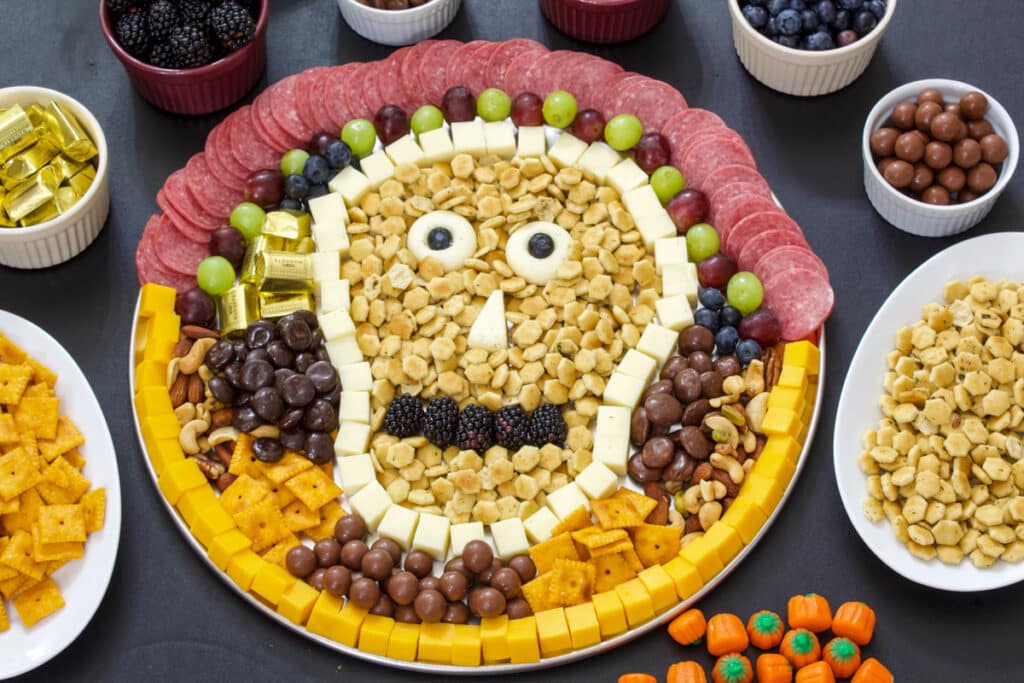 A large round tray with a fun and easy Halloween charcuterie board with additional items around it.
