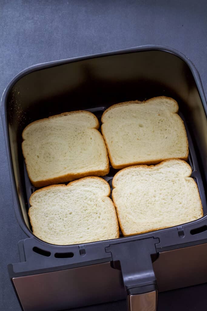 Four pieces of white bread in the air fryer basket before being cooked.