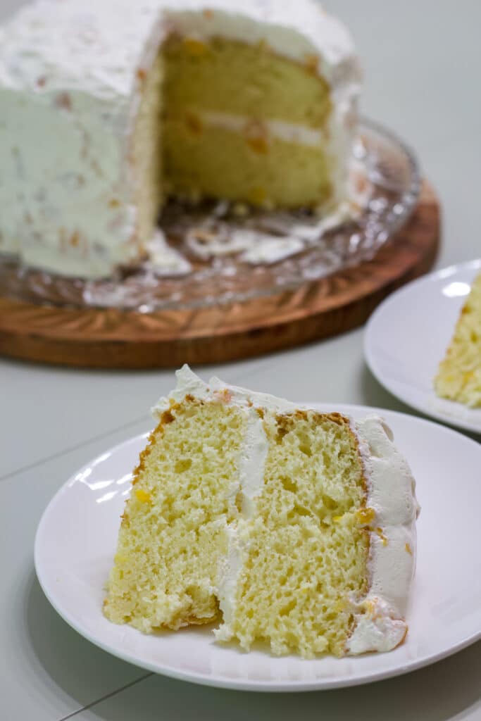 One piece of Peach Cake on a white plate in the foreground and the remaining cake in the background.