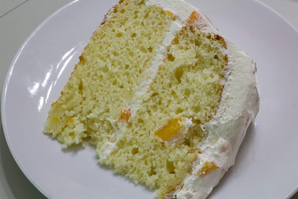 One piece of Peach Cake topped with Canned Peaches and Cool Whip on a white plate.