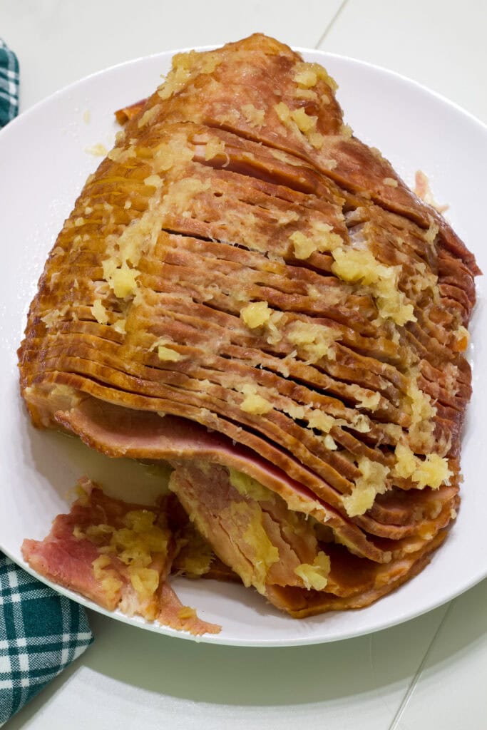 The whole spiral ham on a white plate with a green and white plaid napkin next to it.