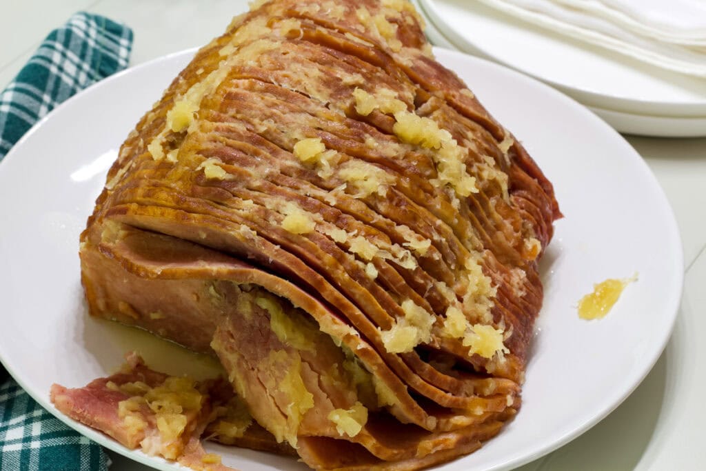The whole cooked spiral ham with pineapple on it on a white plate.