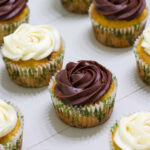 Feature image of several cupcakes on the table, some with chocolate frosting and some with cream cheese frosting.
